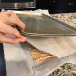 Sandwiching the bacon in between two pans to bake, taken by Allspice Photography, LLC.