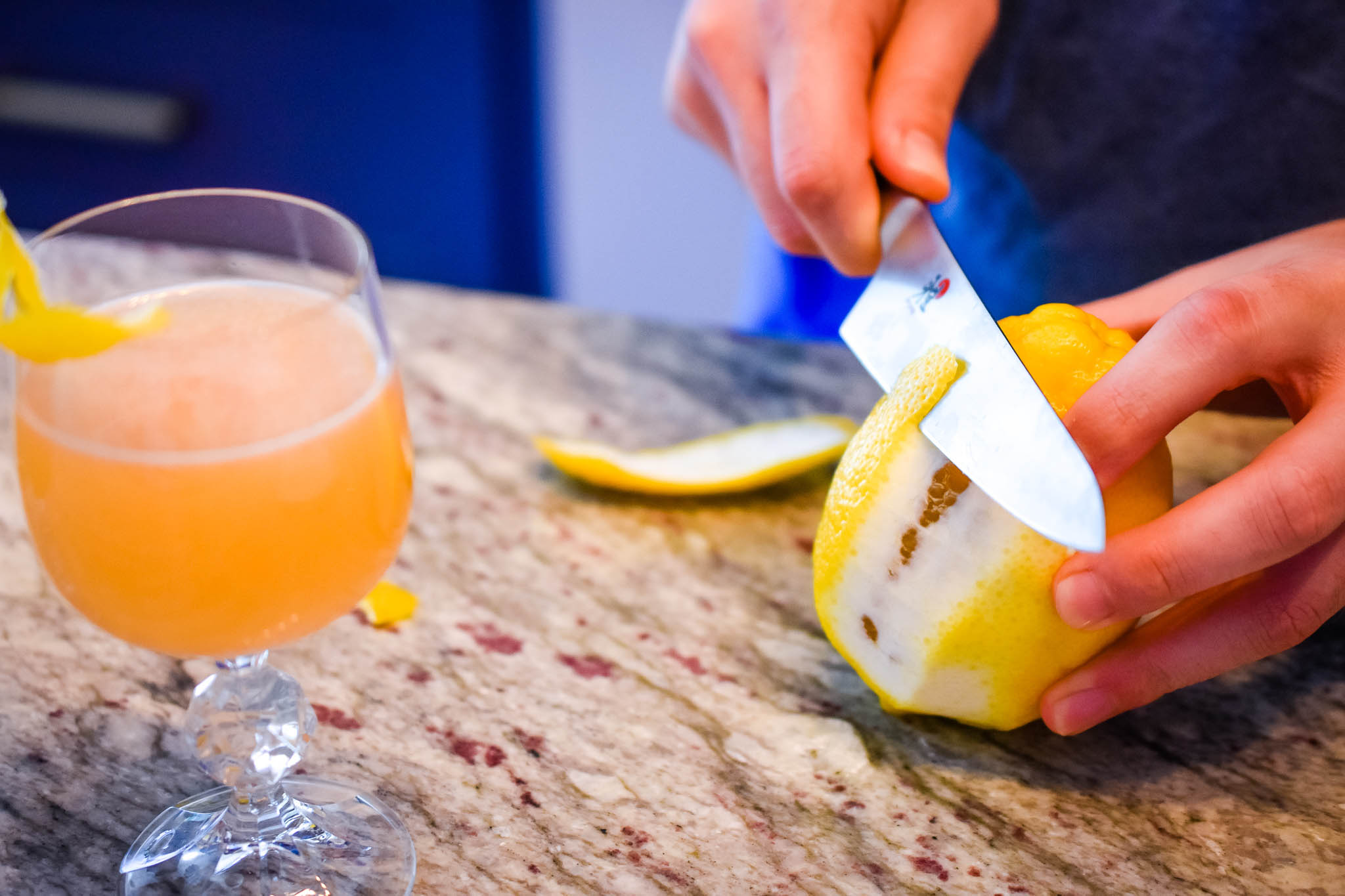 He cuts the lemon peel for our garnish by carefully cutting a small slice of it away and against the rind. Taken by Allspice Photography, LLC.